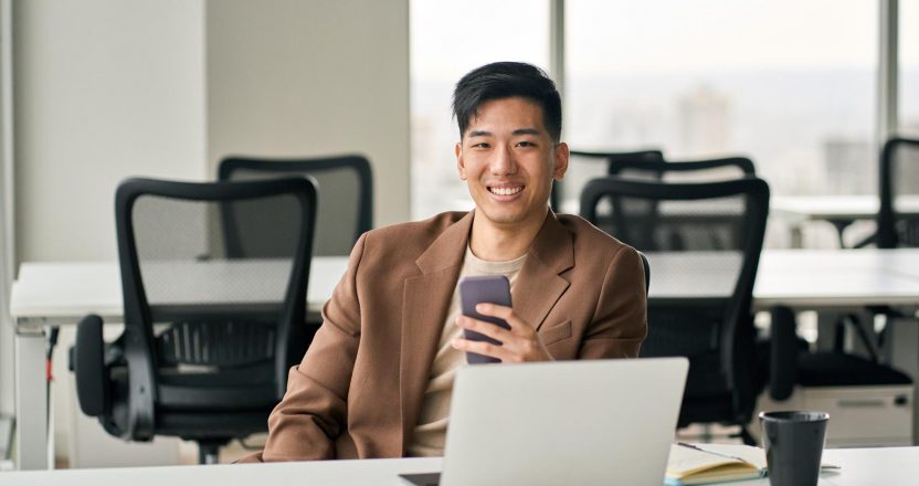 Young happy smiling Asian business man using cell phone in office.