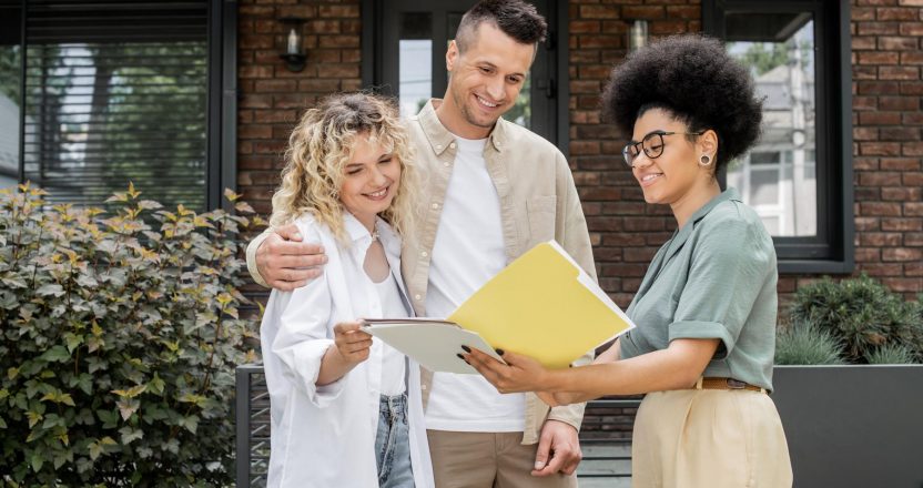 african american property realtor showing documents to happy couple near new modern cottage