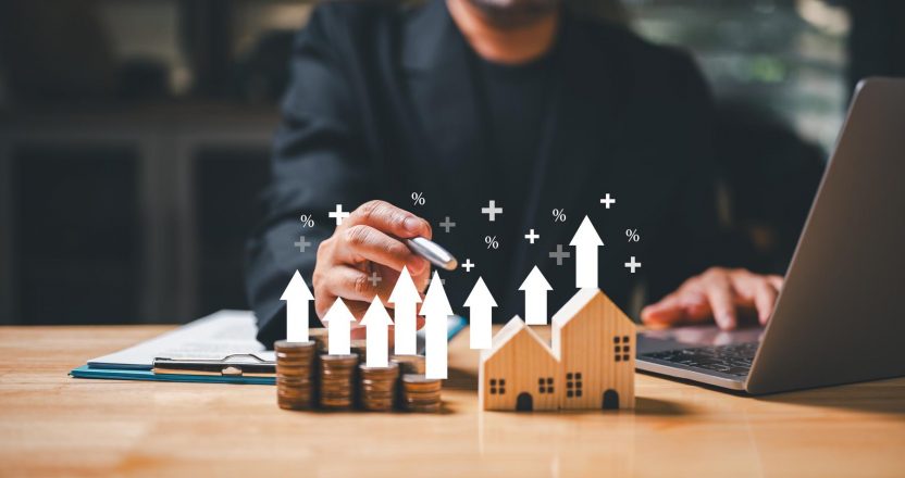 A businessman holding a coin in his hand ponders the concept of wealth and financial security as he looks at a house model, representing the potential investment of a mortgage loan.