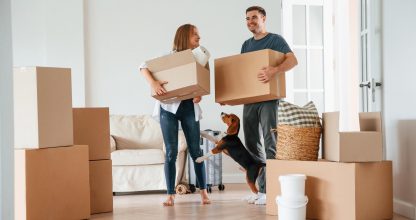 Two boxes in hands. Young couple with dog are moving to new home