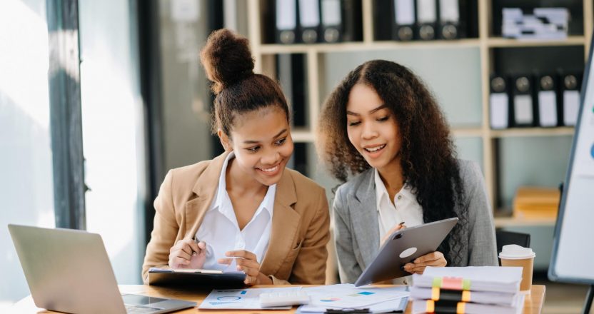 Two African businesswoman discuss investment project working and planning strategy with tablet laptop computer in office.