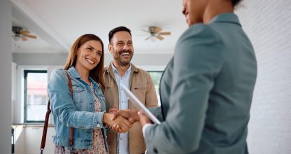 Happy woman shaking hands with real estate agent while buy new home with her husband.