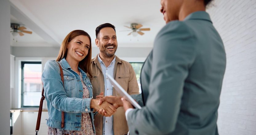 Happy woman shaking hands with real estate agent while buy new home with her husband.