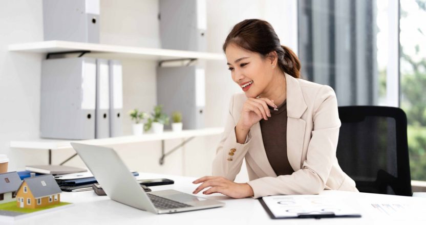 A woman works on a laptop researching the benefits and taxes of rental properties for passive income.