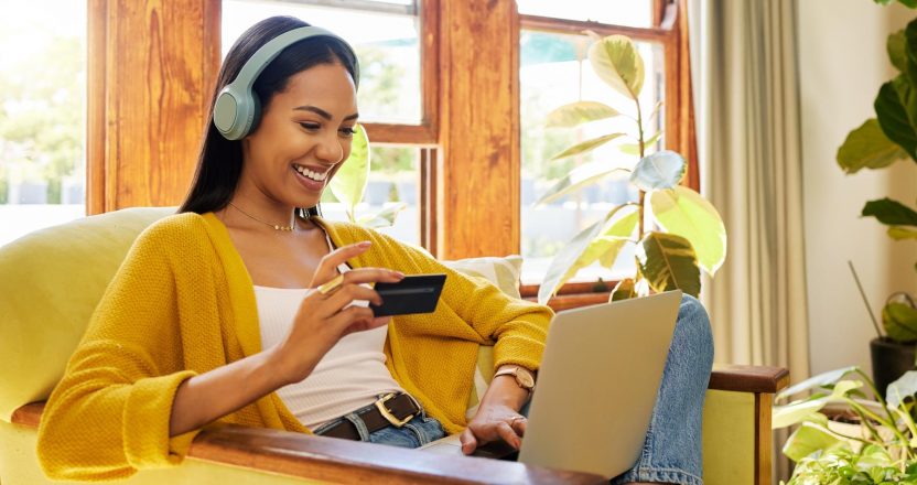 Happy woman, laptop and credit card with ecommerce and headphones to listen to music while online shopping. Female relax at home, radio streaming with fintech, internet banking and payment success