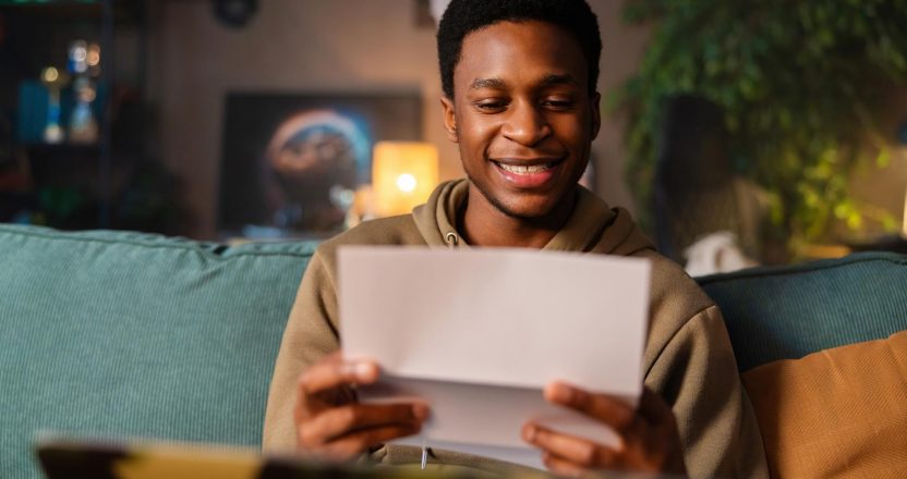 A smiling young man sitting on a couch, reviewing his positive landlord recommendation letter.