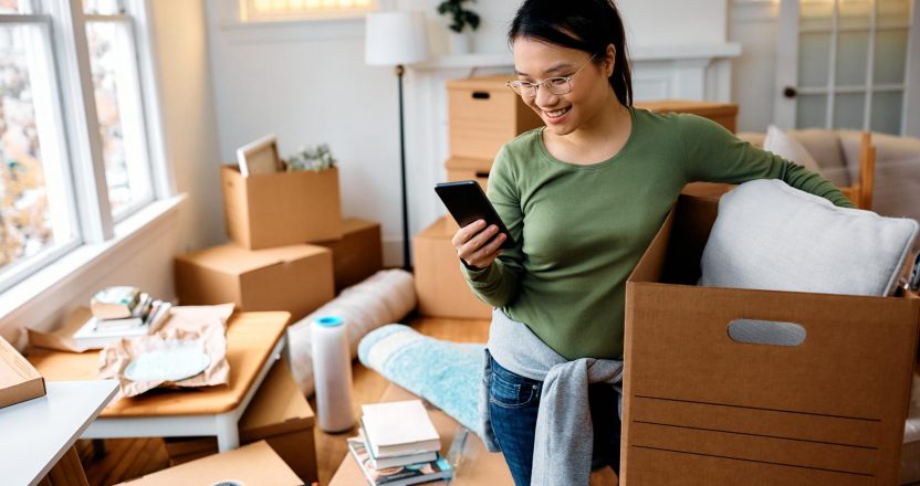 A woman sitting on a sofa, using her phone as she searches for renters insurance.