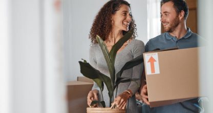 Moving, new home or happy couple with boxes in real estate, property or rental apartment. Woman, proud man or excited people walking together carrying or lifting package in a house on loan with smile