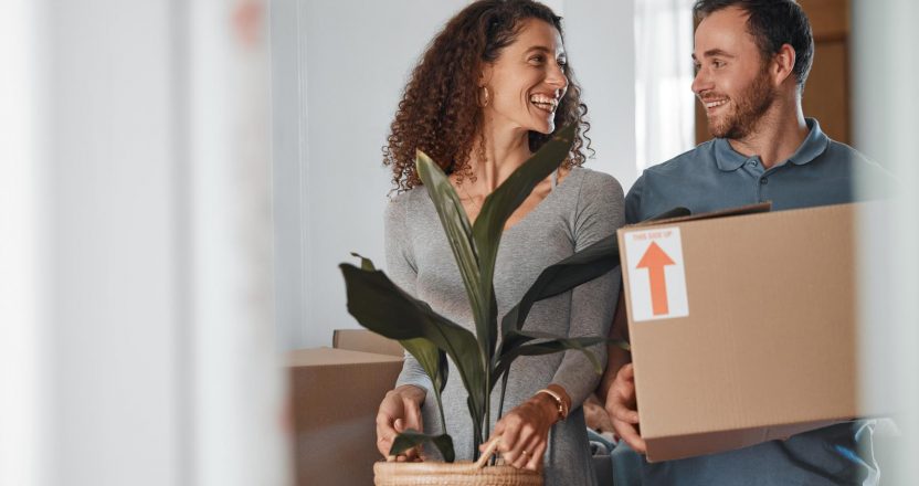 A couple is shown moving into a house, carrying a plant and a cardboard box.