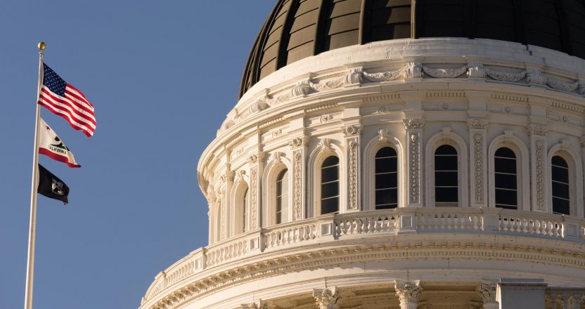 Three flags fly beside the Capitol's white dome in Sacramento, where lawmakers set California's rent application rules.