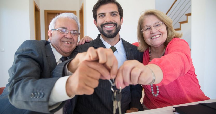 Smiling elderly couple holding house keys along with their property manager indoors.