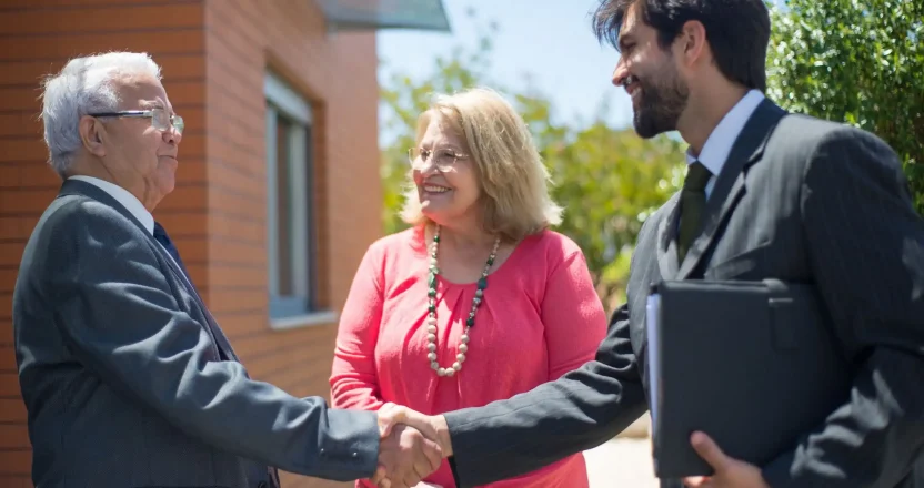 A property manager and elderly couple shaking hands outdoors, sealing a deal with smiles.