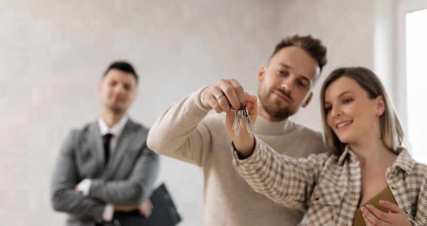 A joyful couple holding keys to their new home with a property manager in the background.